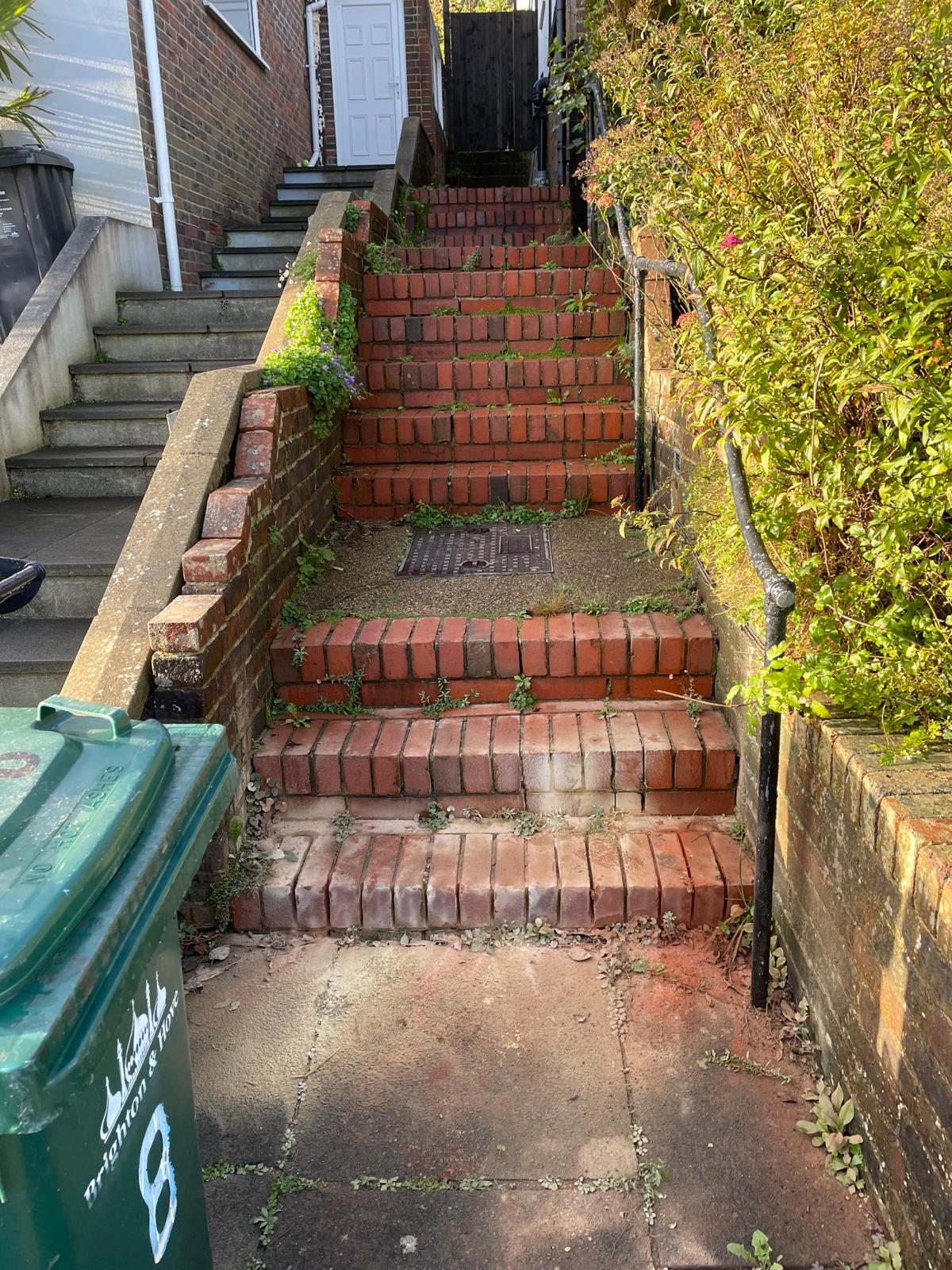 Overgrown brick steps with loose bricks and weeds